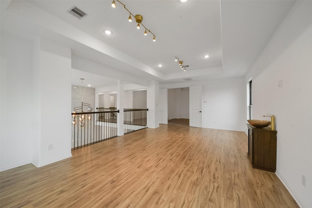 unfurnished room with a tray ceiling, light wood finished floors, recessed lighting, rail lighting, and visible vents