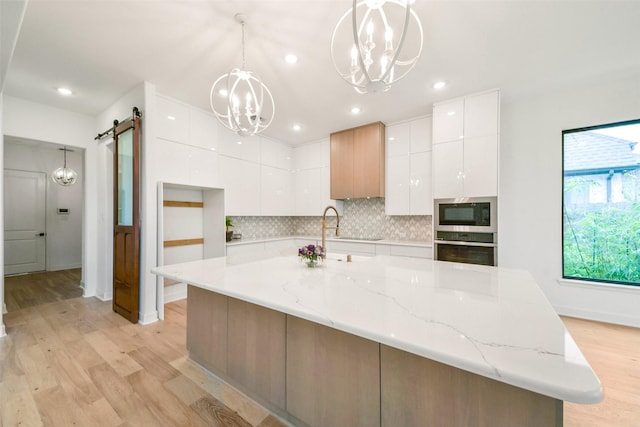 kitchen with a barn door, white cabinetry, appliances with stainless steel finishes, modern cabinets, and an inviting chandelier