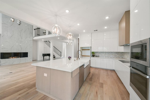 kitchen featuring a fireplace, appliances with stainless steel finishes, light wood-style floors, white cabinets, and modern cabinets