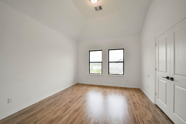 empty room featuring lofted ceiling, light wood-style flooring, visible vents, and baseboards