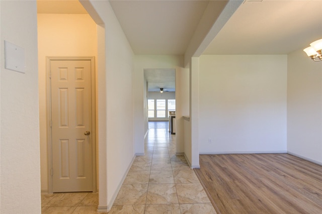 hallway with a notable chandelier, light wood-style flooring, and baseboards