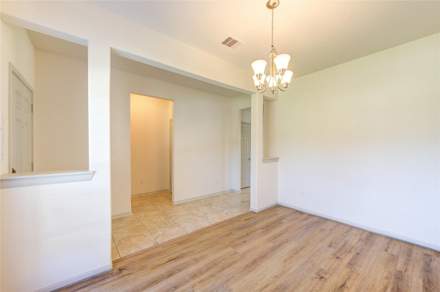 empty room featuring a chandelier, wood finished floors, visible vents, and baseboards