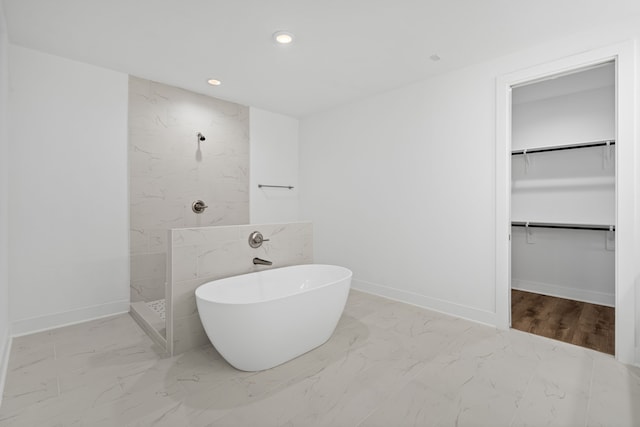 full bath featuring a walk in shower, a walk in closet, a freestanding bath, and marble finish floor