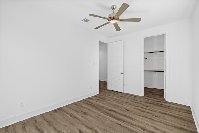 unfurnished bedroom with wood finished floors, a ceiling fan, a walk in closet, visible vents, and baseboards