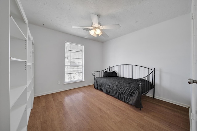 bedroom with a textured ceiling, baseboards, and wood finished floors