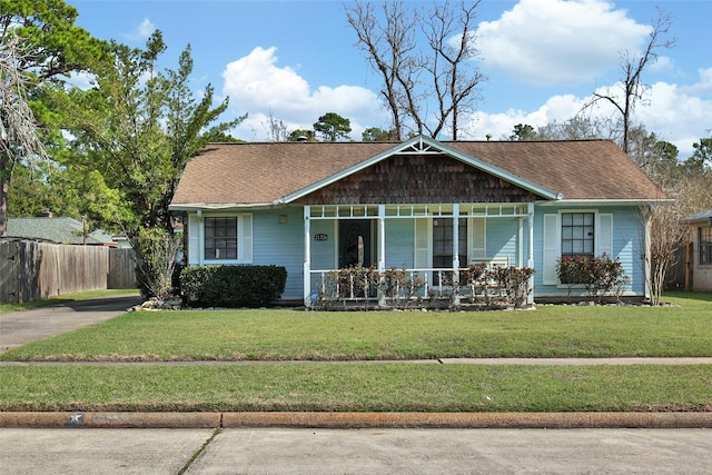 view of front of home with roof with shingles, a porch, a front lawn, and fence