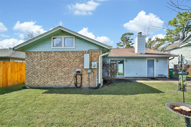 rear view of house with brick siding, fence, a chimney, and a lawn