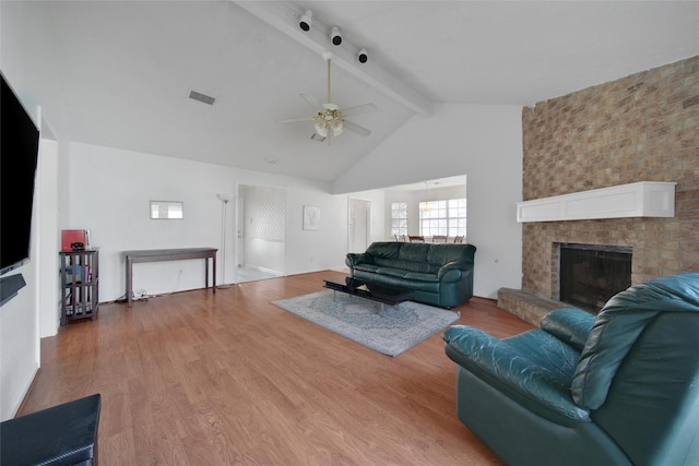 living area featuring ceiling fan, high vaulted ceiling, light wood-style flooring, a fireplace, and beamed ceiling