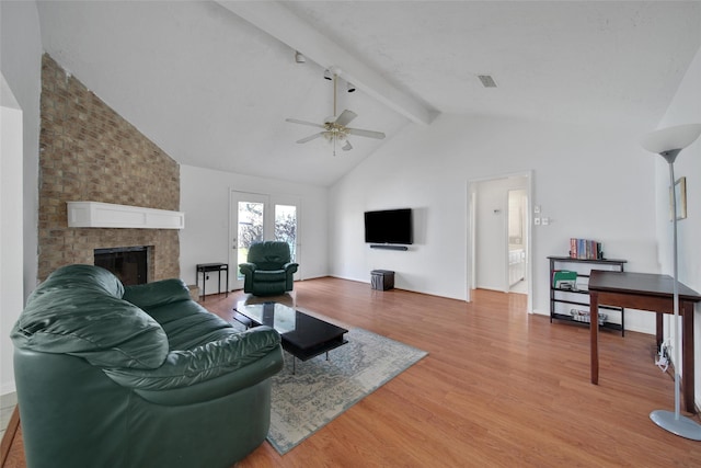 living room featuring light wood-style flooring, a fireplace, visible vents, a ceiling fan, and beamed ceiling