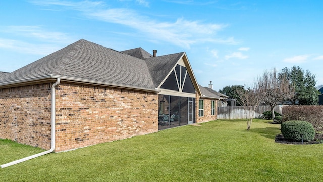 back of house featuring brick siding, a shingled roof, a lawn, a sunroom, and fence