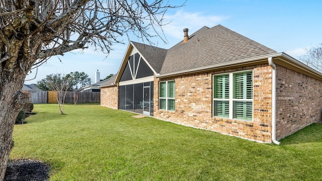 rear view of property featuring roof with shingles, brick siding, a lawn, and fence