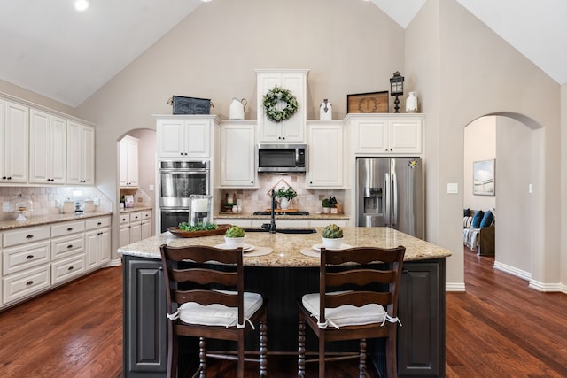 kitchen with high vaulted ceiling, appliances with stainless steel finishes, arched walkways, and dark wood finished floors