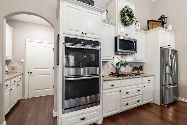 kitchen with arched walkways, dark wood-style floors, appliances with stainless steel finishes, white cabinetry, and backsplash