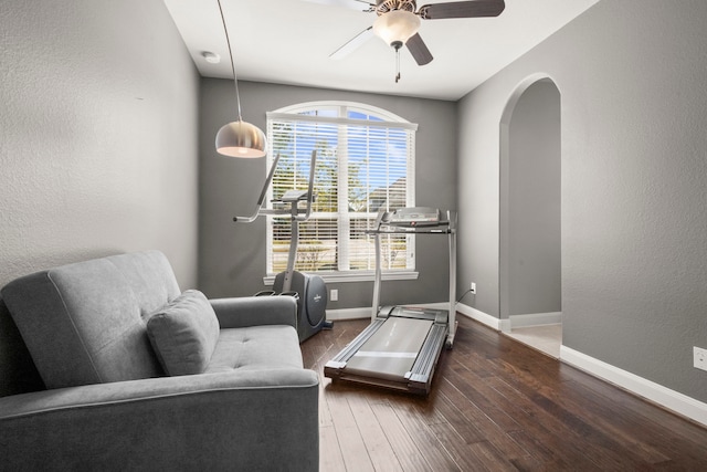 living area with arched walkways, a textured wall, a ceiling fan, wood finished floors, and baseboards