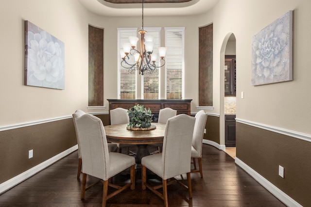 dining space featuring arched walkways, dark wood-type flooring, a notable chandelier, and baseboards