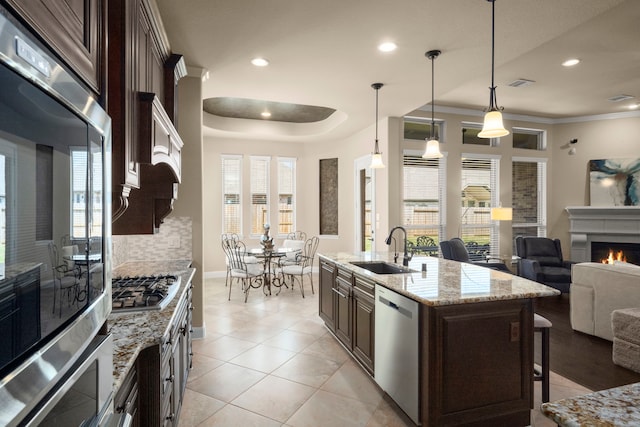 kitchen featuring a warm lit fireplace, stainless steel appliances, a sink, a kitchen breakfast bar, and dark brown cabinets