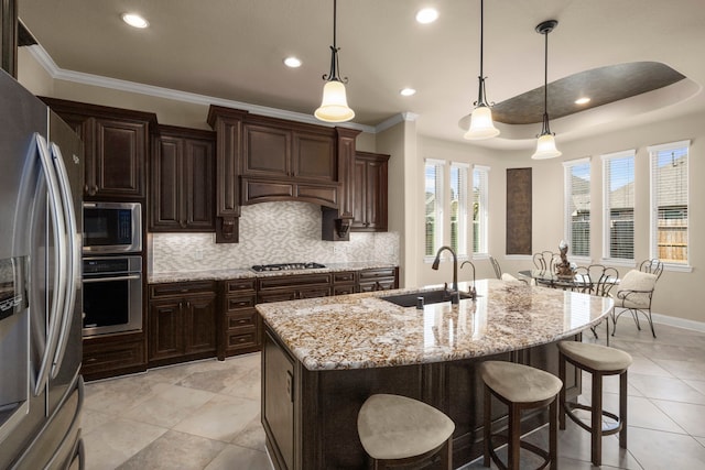 kitchen featuring a breakfast bar area, tasteful backsplash, appliances with stainless steel finishes, a sink, and light stone countertops