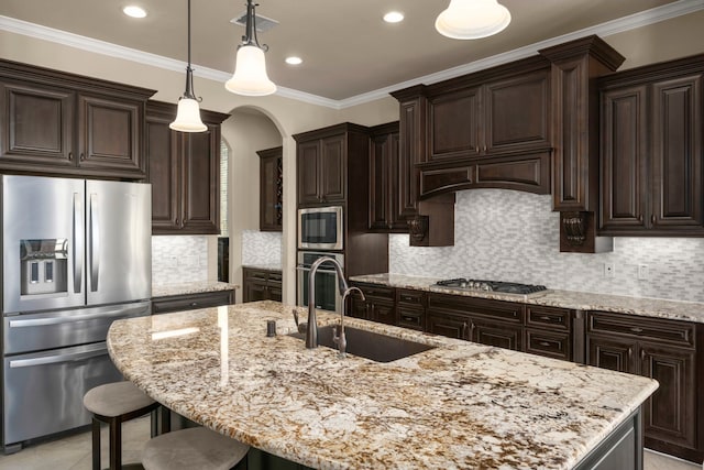 kitchen with arched walkways, appliances with stainless steel finishes, ornamental molding, dark brown cabinets, and a sink