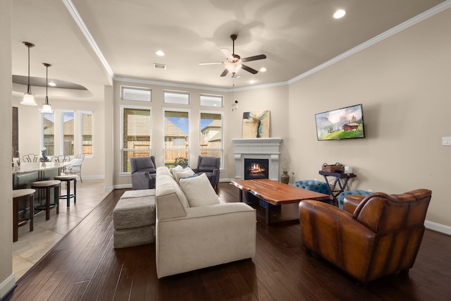 living area with visible vents, ornamental molding, a warm lit fireplace, plenty of natural light, and hardwood / wood-style flooring