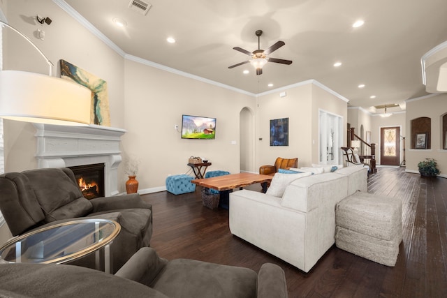 living room featuring a warm lit fireplace, visible vents, arched walkways, and ornamental molding