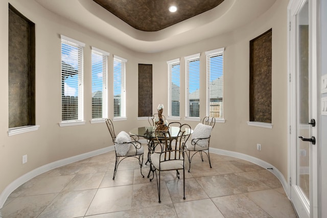 dining space featuring baseboards, a raised ceiling, and light tile patterned flooring