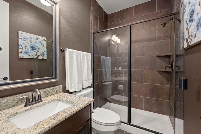 bathroom featuring toilet, a stall shower, a textured wall, and vanity