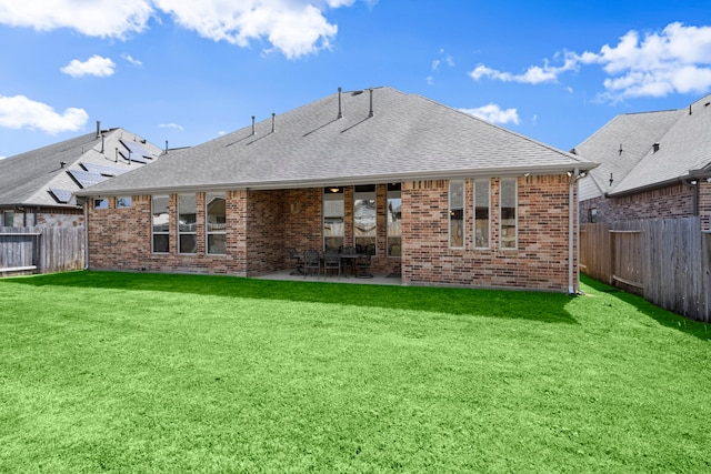 back of house featuring a shingled roof, a lawn, a fenced backyard, and brick siding