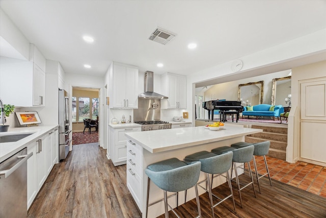 kitchen featuring a breakfast bar area, stainless steel appliances, visible vents, light countertops, and wall chimney range hood