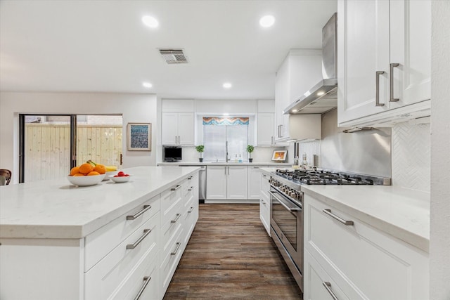 kitchen featuring visible vents, appliances with stainless steel finishes, dark wood-type flooring, a sink, and wall chimney exhaust hood