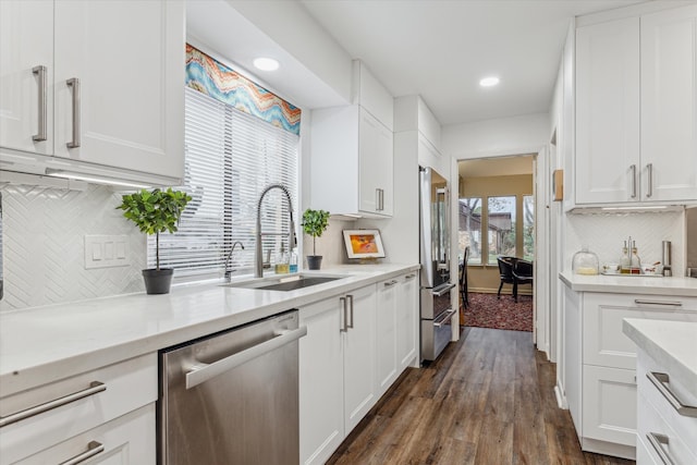 kitchen with a sink, white cabinetry, appliances with stainless steel finishes, backsplash, and dark wood-style floors