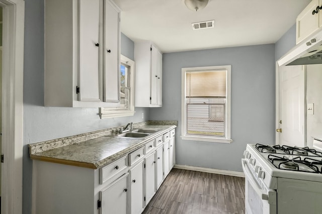 kitchen featuring white range with gas cooktop, visible vents, under cabinet range hood, white cabinetry, and a sink