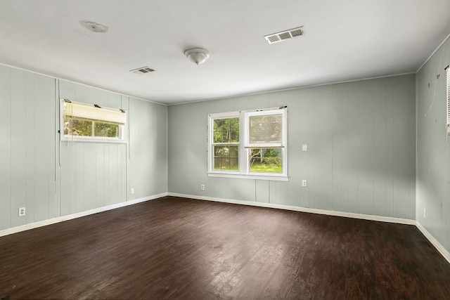 empty room with dark wood-style floors, visible vents, and baseboards