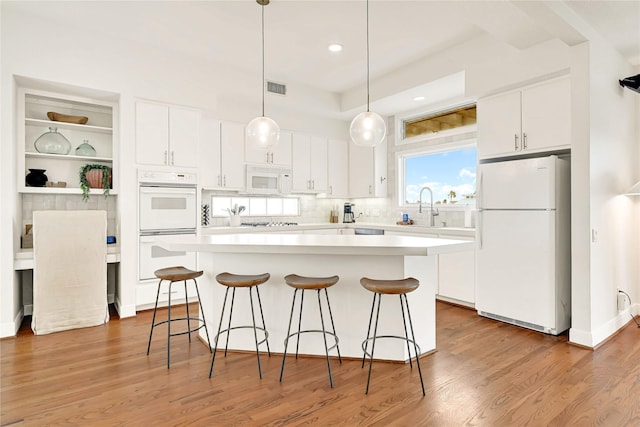 kitchen with visible vents, white cabinets, wood finished floors, white appliances, and a kitchen bar