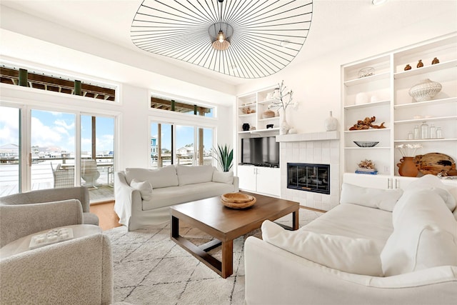 living area with built in shelves, a tiled fireplace, and wood finished floors