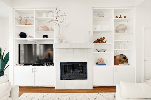 living area with built in features, a tiled fireplace, and wood finished floors