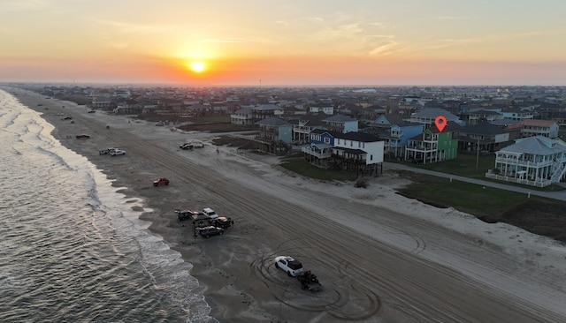 aerial view at dusk featuring a view of the beach and a water view