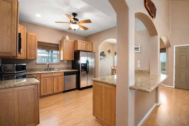 kitchen featuring appliances with stainless steel finishes, a sink, light wood-style floors, and light stone countertops