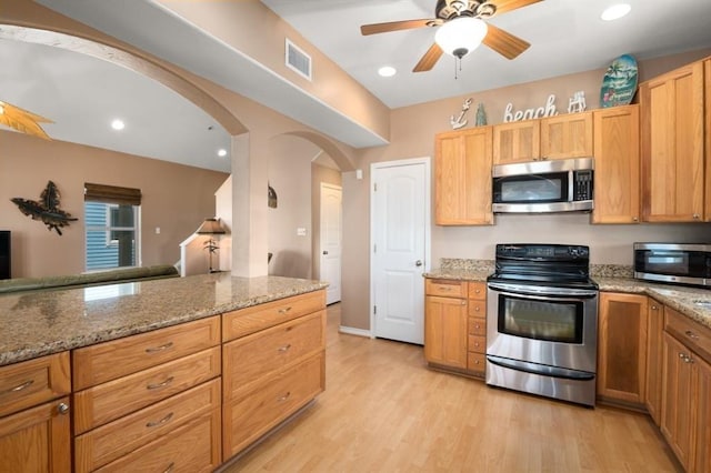 kitchen with light wood finished floors, visible vents, arched walkways, light stone counters, and stainless steel appliances