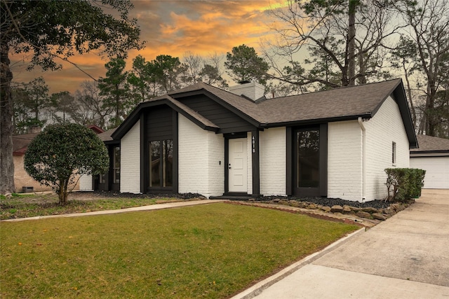 view of front of home featuring a garage, brick siding, a yard, roof with shingles, and a chimney