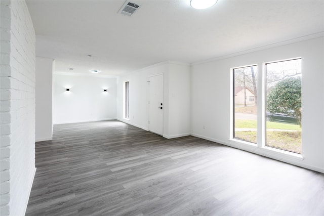 spare room with plenty of natural light, visible vents, wood finished floors, and ornamental molding