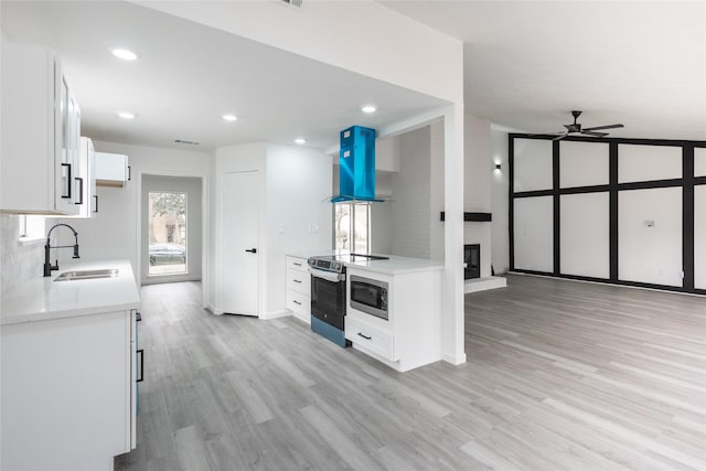 kitchen with island range hood, a sink, white cabinetry, appliances with stainless steel finishes, and light wood-type flooring