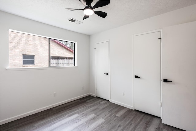 unfurnished bedroom with baseboards, a textured ceiling, visible vents, and wood finished floors