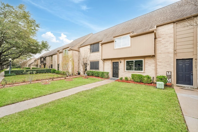 view of property featuring a shingled roof, brick siding, and a front lawn