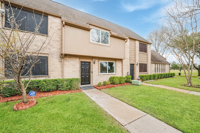 multi unit property with brick siding, a front yard, and a shingled roof