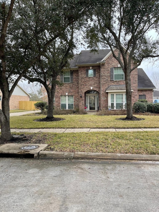 view of front of home with brick siding, a front yard, and fence