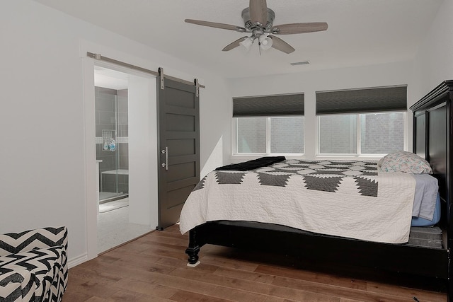 bedroom with a ceiling fan, wood finished floors, visible vents, a barn door, and connected bathroom