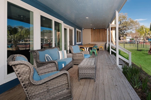 wooden terrace with an outdoor living space, a lawn, and fence