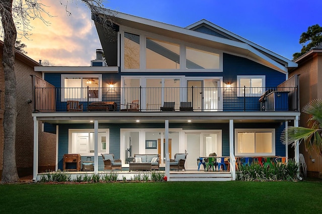 back of property with a balcony, a porch, and a lawn