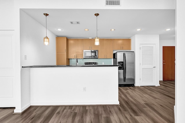 kitchen featuring stainless steel appliances, a peninsula, visible vents, dark countertops, and dark wood finished floors