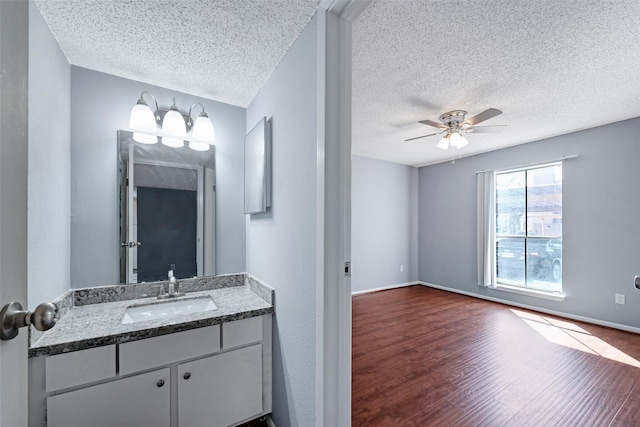 bathroom featuring ceiling fan, vanity, a textured ceiling, wood finished floors, and baseboards